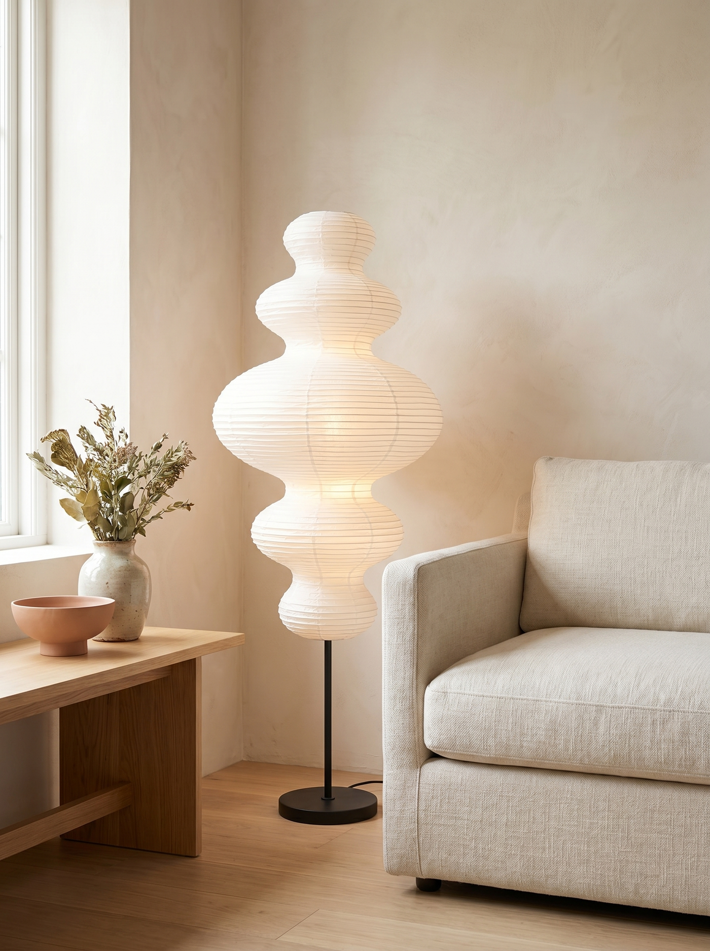 White paper gourd floor lamp lit beside a sofa in a warm daylit living room