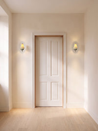 A pair of chrome pleated ceramic wall sconces flanking a door in a daylit hallway