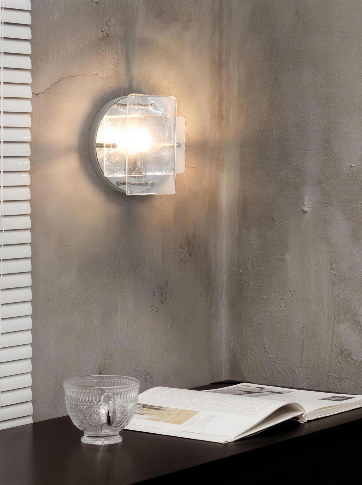Ice-pattern glass wall sconce lit on a wall in a daylit room
