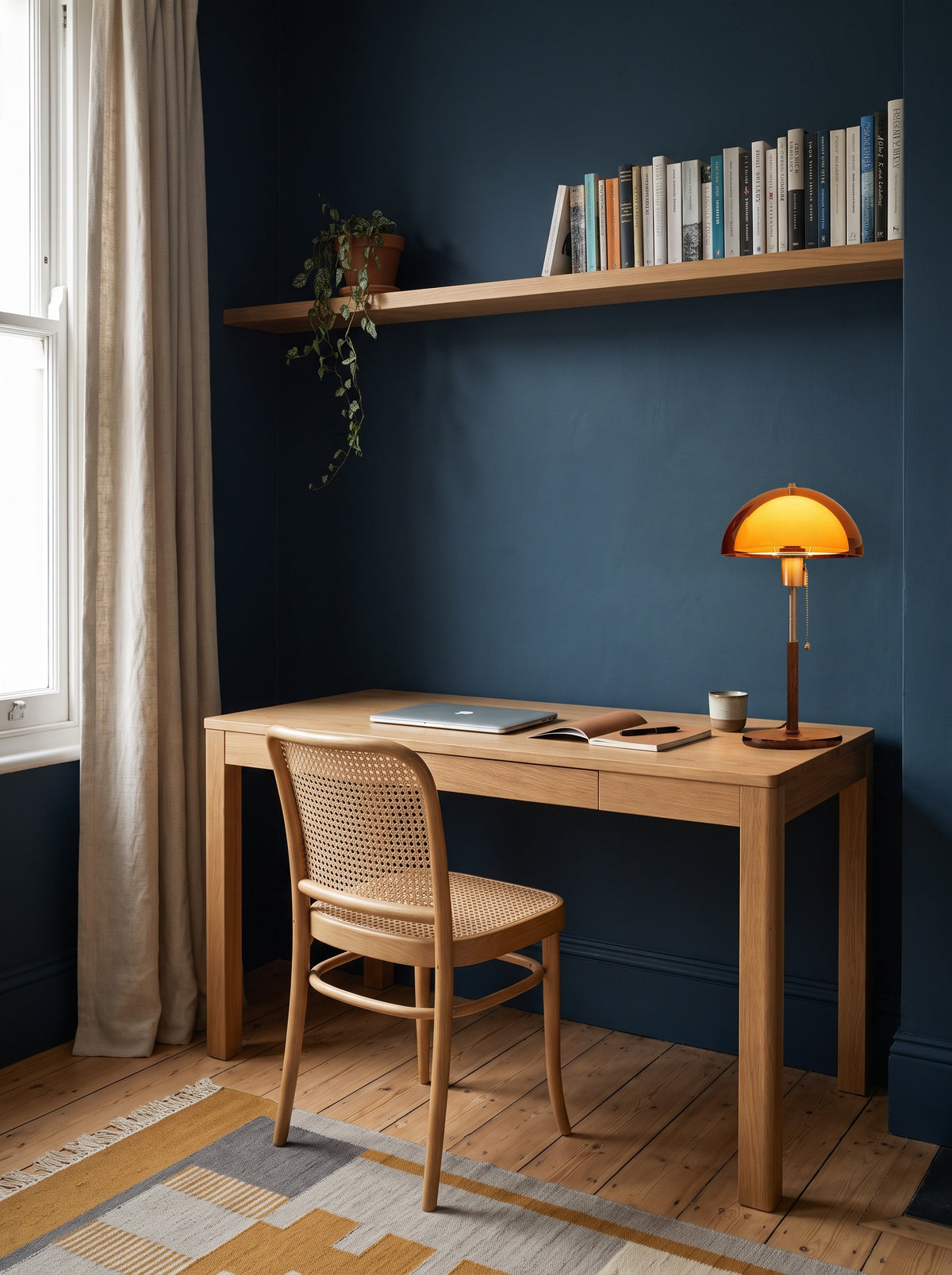 Amber dome table lamp switched on at the end of an oak desk in a daylit ink-blue home study