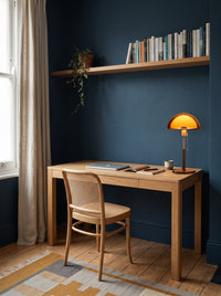 Amber dome table lamp switched on at the end of an oak desk in a daylit ink-blue home study