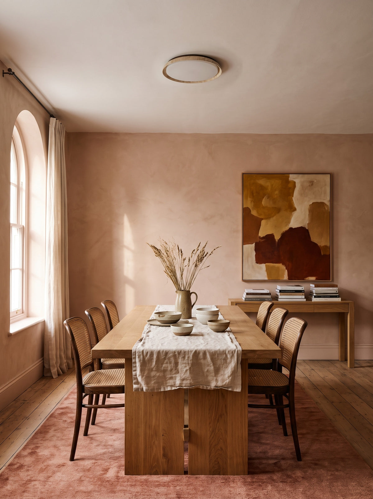 Travertine wabi-sabi ceiling light above a dining table in a daylit clay-pink dining room