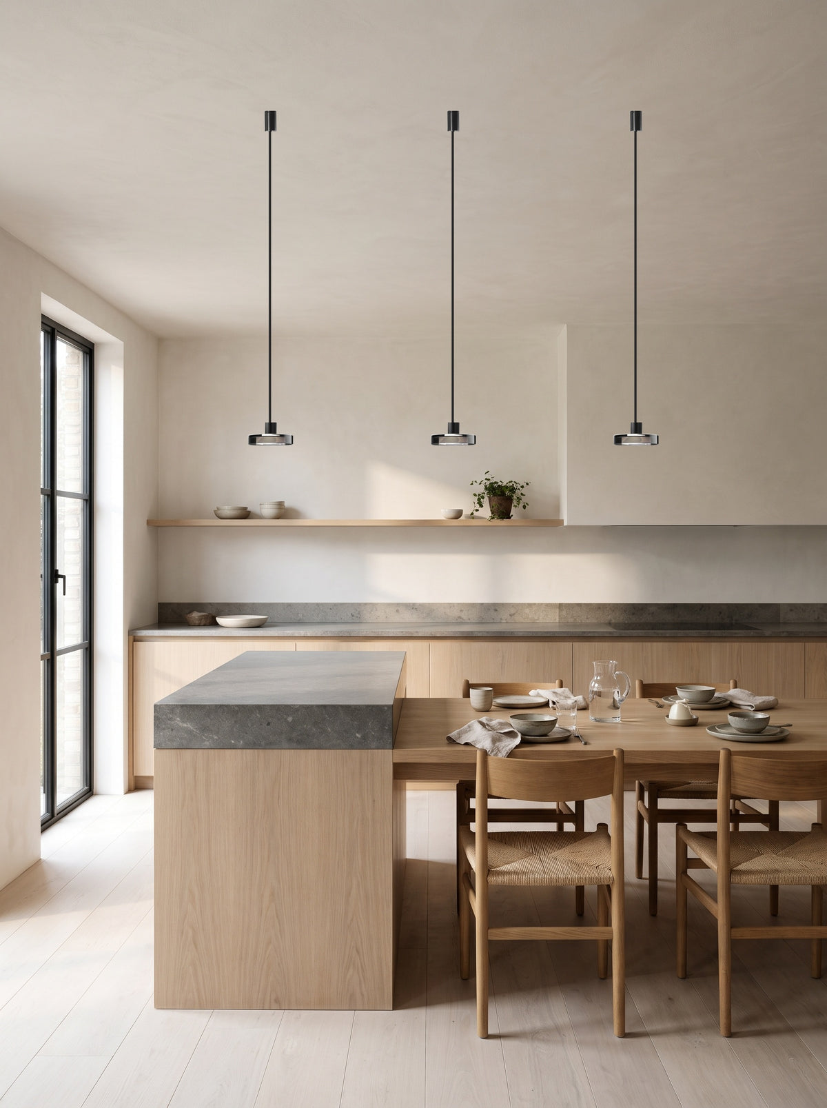 Three smoke grey glass pendant lights in a row above a kitchen island and dining table in a daylit oak kitchen