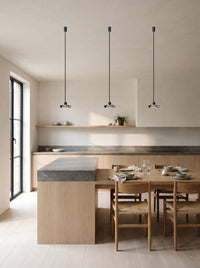Three smoke grey glass pendant lights in a row above a kitchen island and dining table in a daylit oak kitchen