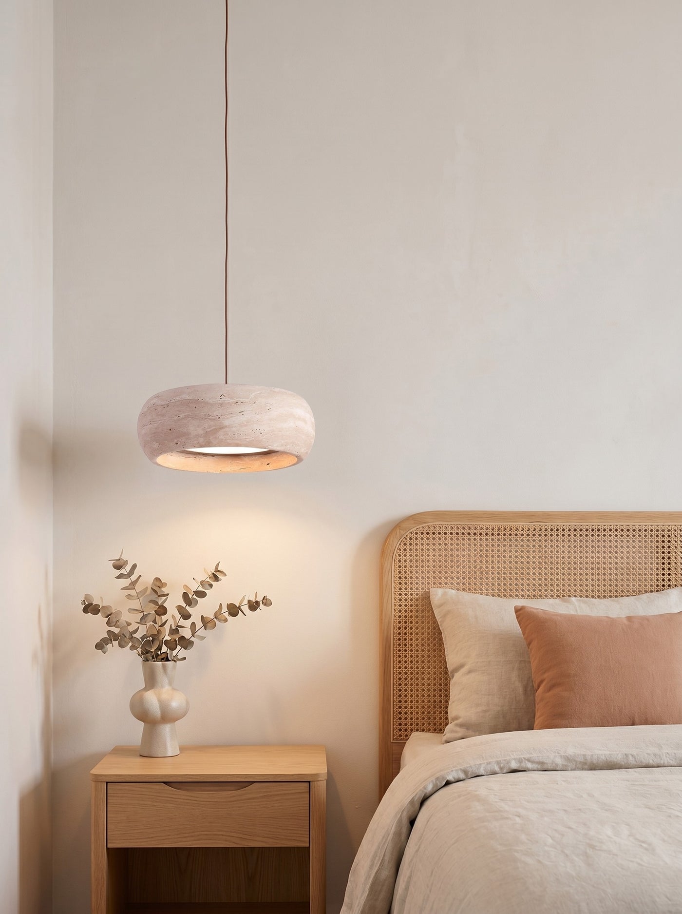 Travertine drum pendant glowing softly above a nightstand in a daylit Japandi bedroom