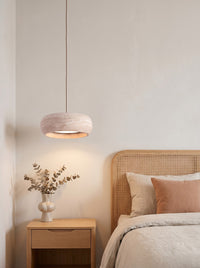 Travertine drum pendant glowing softly above a nightstand in a daylit Japandi bedroom