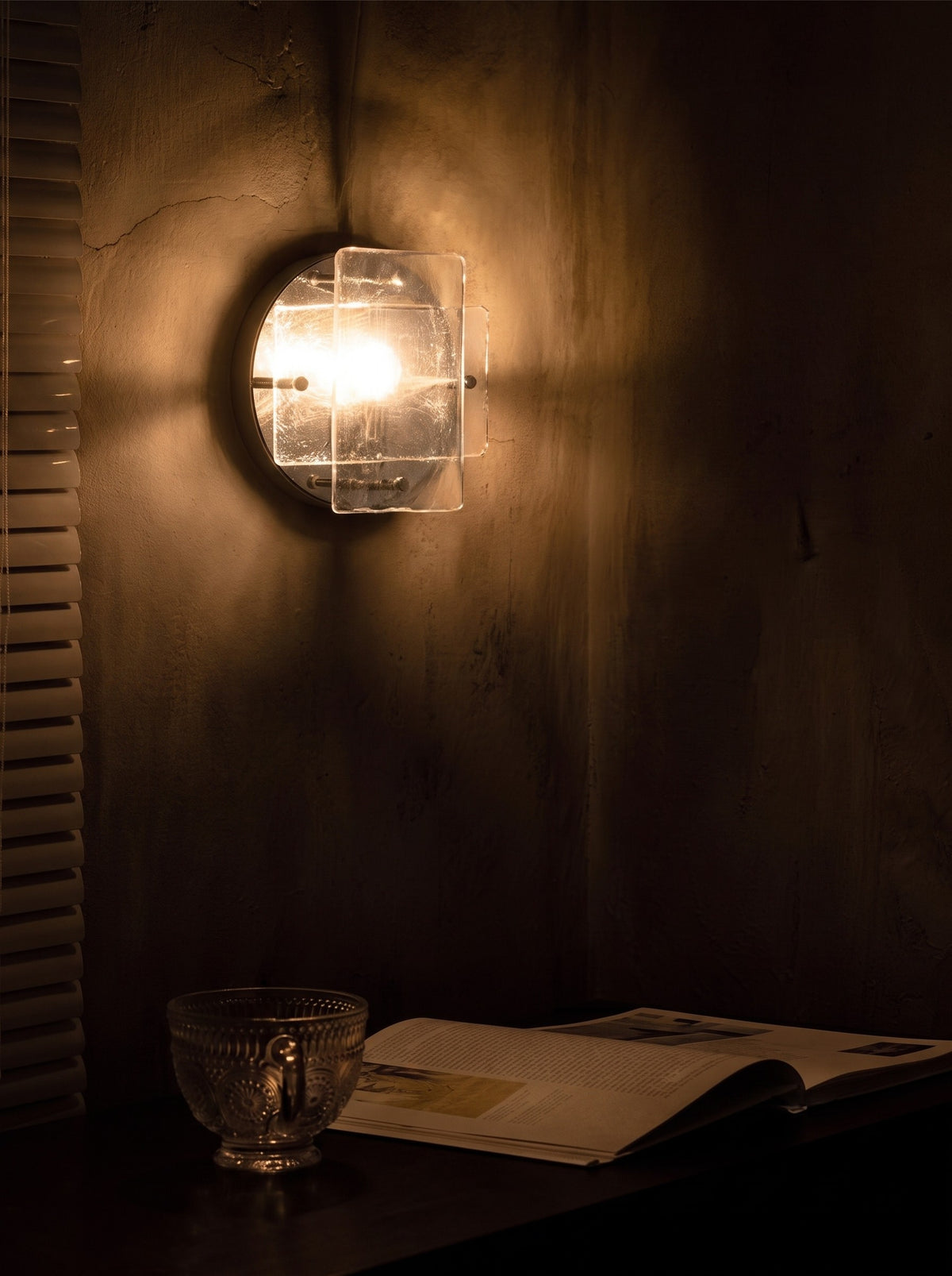 Ice-pattern glass wall sconce glowing on a wall in a dark room at night