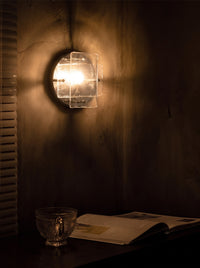 Ice-pattern glass wall sconce glowing on a wall in a dark room at night