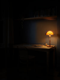 Amber dome table lamp as the only light on an oak desk in a dark home study at night