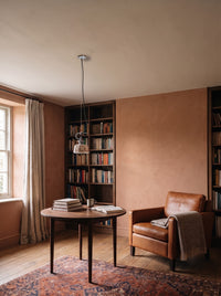 Hand-painted ceramic pendant light over a round reading table in a daylit terracotta reading corner