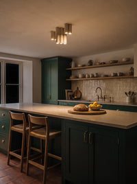 A cluster of seven travertine cylinder ceiling lights switched on above an island in a dark kitchen at night