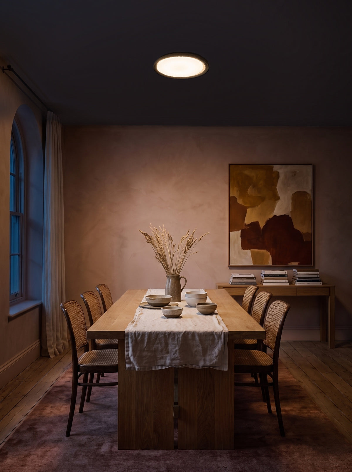 Travertine wabi-sabi ceiling light switched on above a dining table in a dark dining room at night