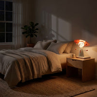 Bedside lamp glowing warm at night, the only light in a dark bedroom, holding glasses and jewelry