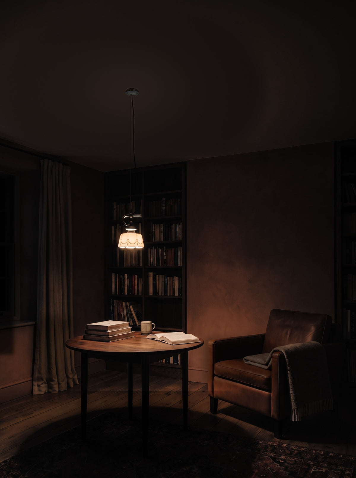 Hand-painted ceramic pendant light switched on over a round reading table in a dark reading corner at night