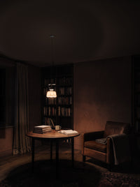 Hand-painted ceramic pendant light switched on over a round reading table in a dark reading corner at night