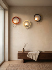 Three fabric disc wall sconces in copper, white and black on a plaster wall in a daylit living room
