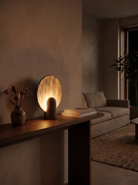Travertine disc table lamp glowing warm at night as the room's main light