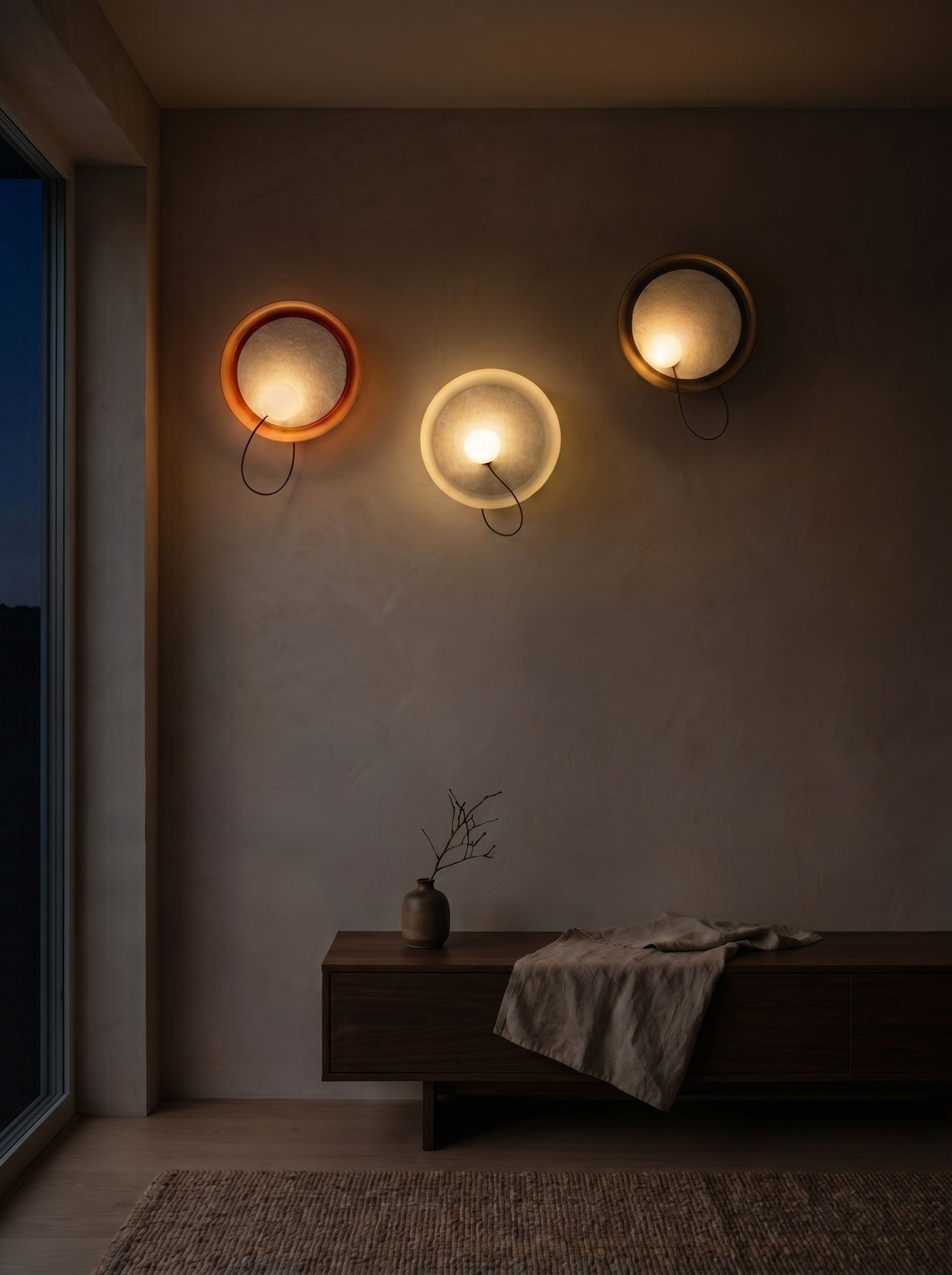 Three fabric disc wall sconces glowing warm on a wall in a dark room at night