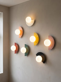 Seven iron half moon wall sconces in different colours arranged on a wall in a daylit room